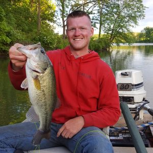 Close up of man wearing a red sweatshirt. He is sitting in a boat on the water and is holding a large bass.