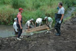 A group of six people on a stream bank placing a pallet in the water.